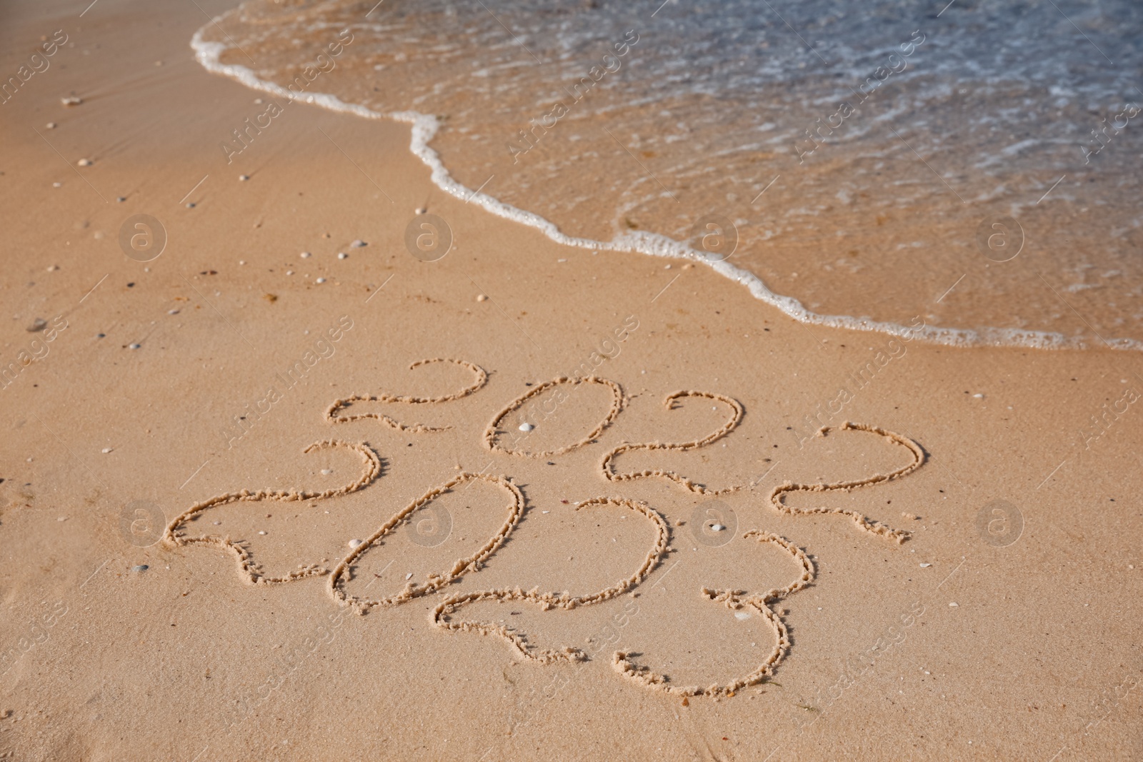 Photo of 2022 and 2023 written on sand at beach. New Year celebration