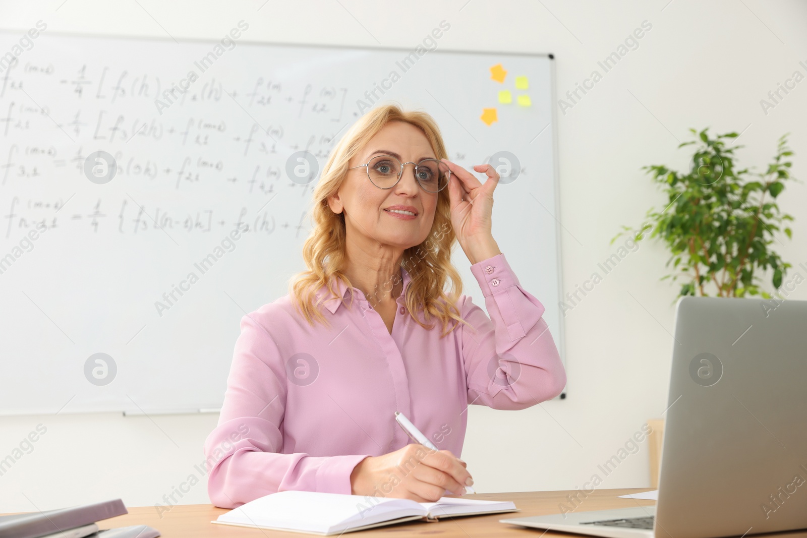 Photo of Teacher giving lesson near laptop at desk in classroom