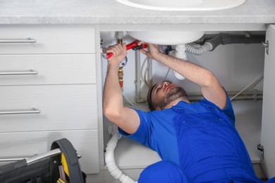 Professional plumber in uniform fixing sink with pipe wrench