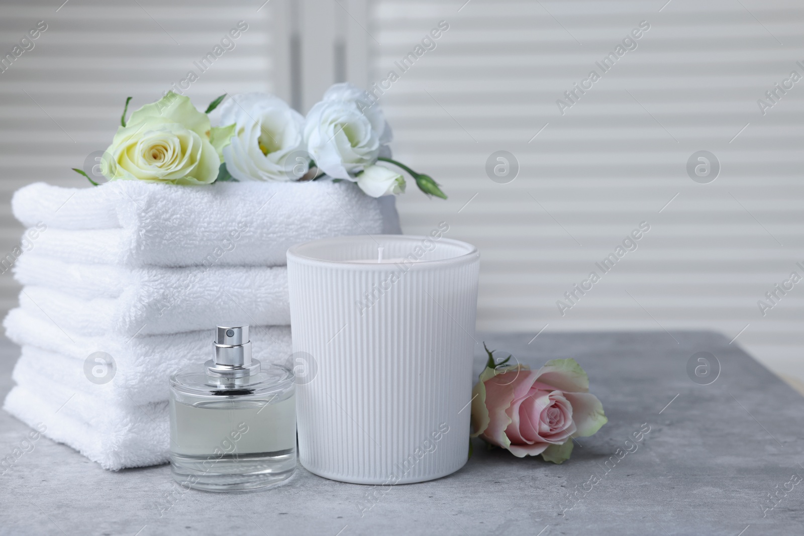 Photo of Towels, bottle of perfume, scented candle and flowers on grey table indoors