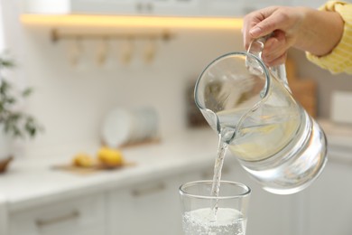 Photo of Woman pouring water from jug into glass in kitchen, closeup. Space for text