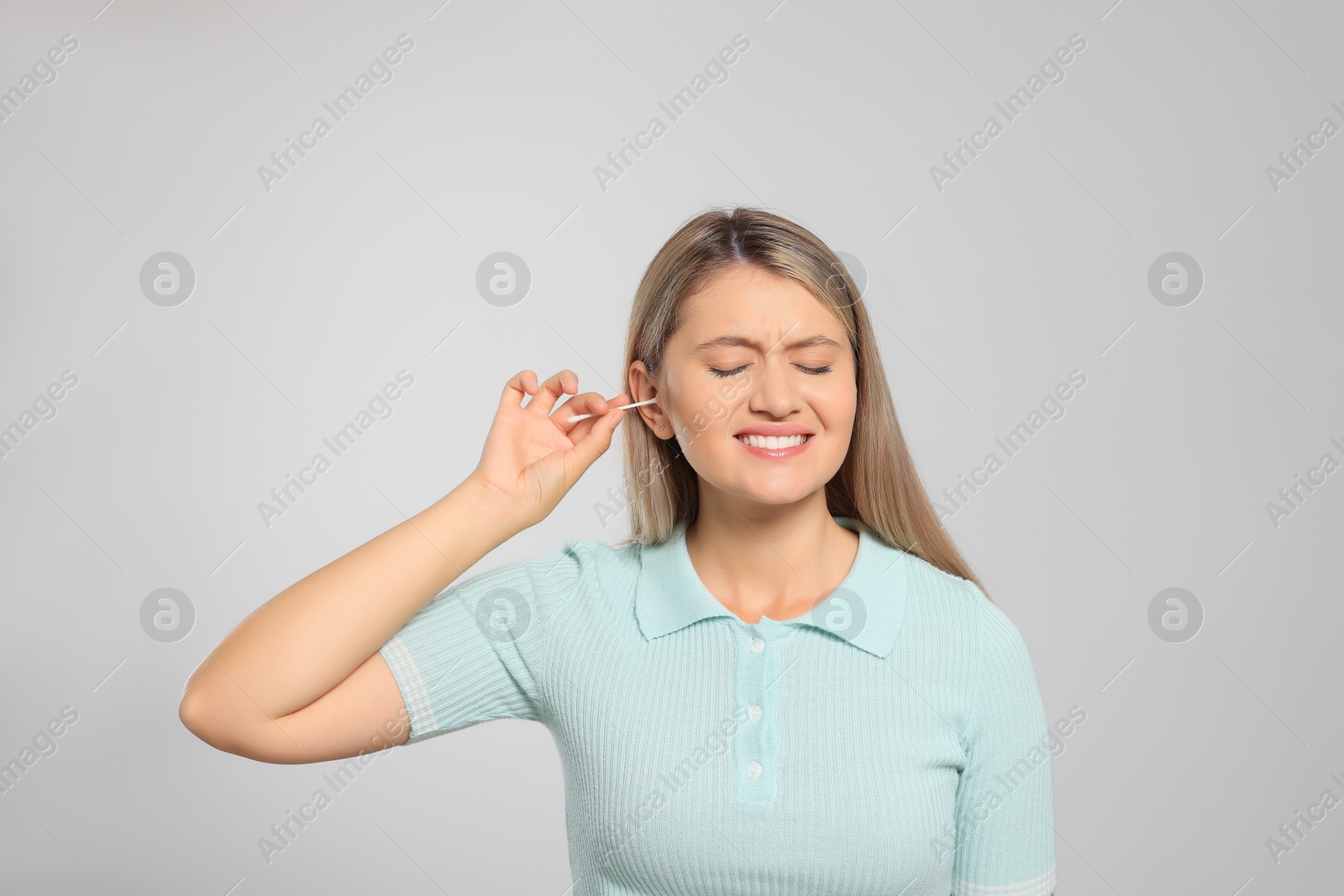 Photo of Young woman cleaning ear with cotton swab on light grey background