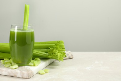 Glass of celery juice and fresh vegetables on light gray table, space for text