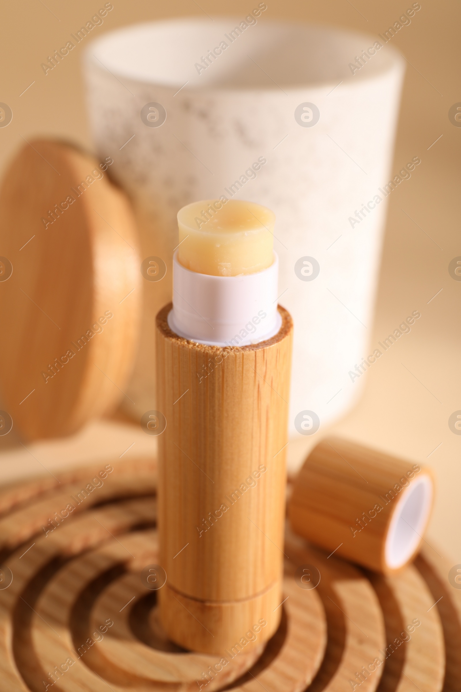 Photo of Lip balm on wooden coaster against blurred background, closeup