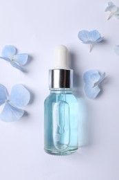 Photo of Bottle of cosmetic serum and beautiful flowers on white background, flat lay