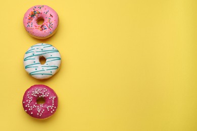 Photo of Tasty glazed donuts on yellow background, top view. Space for text