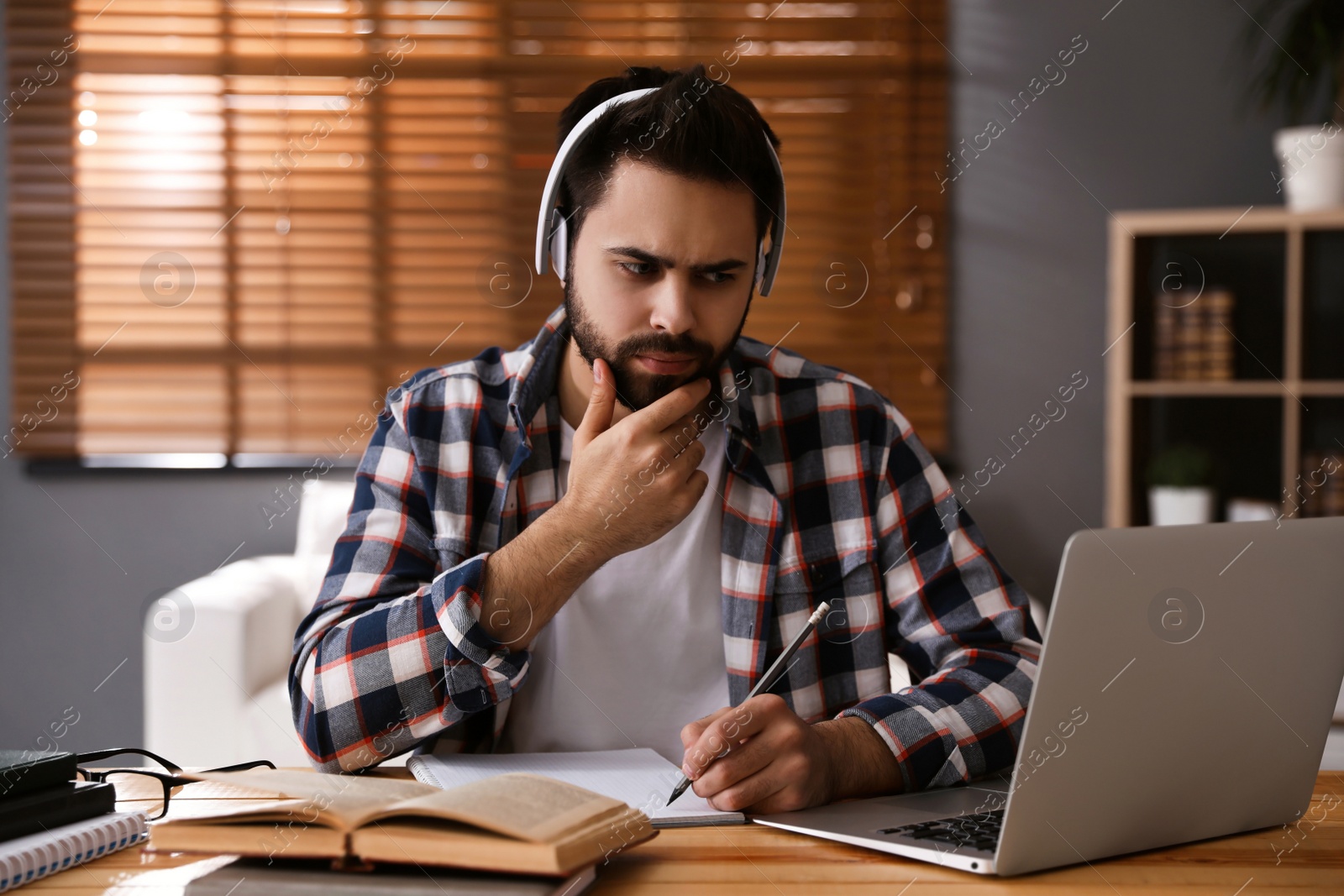 Photo of Confused young man watching webinar at table in room