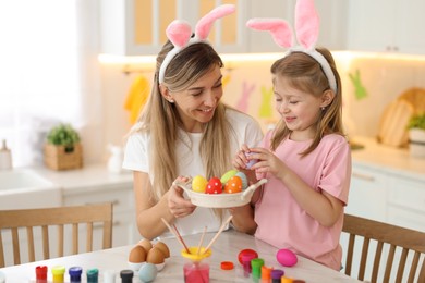 Photo of Easter celebration. Happy mother and her cute daughter with painted eggs at white marble table in kitchen