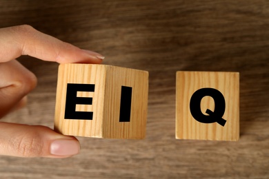 Woman turning cube with letters E and I near Q at wooden table, top view