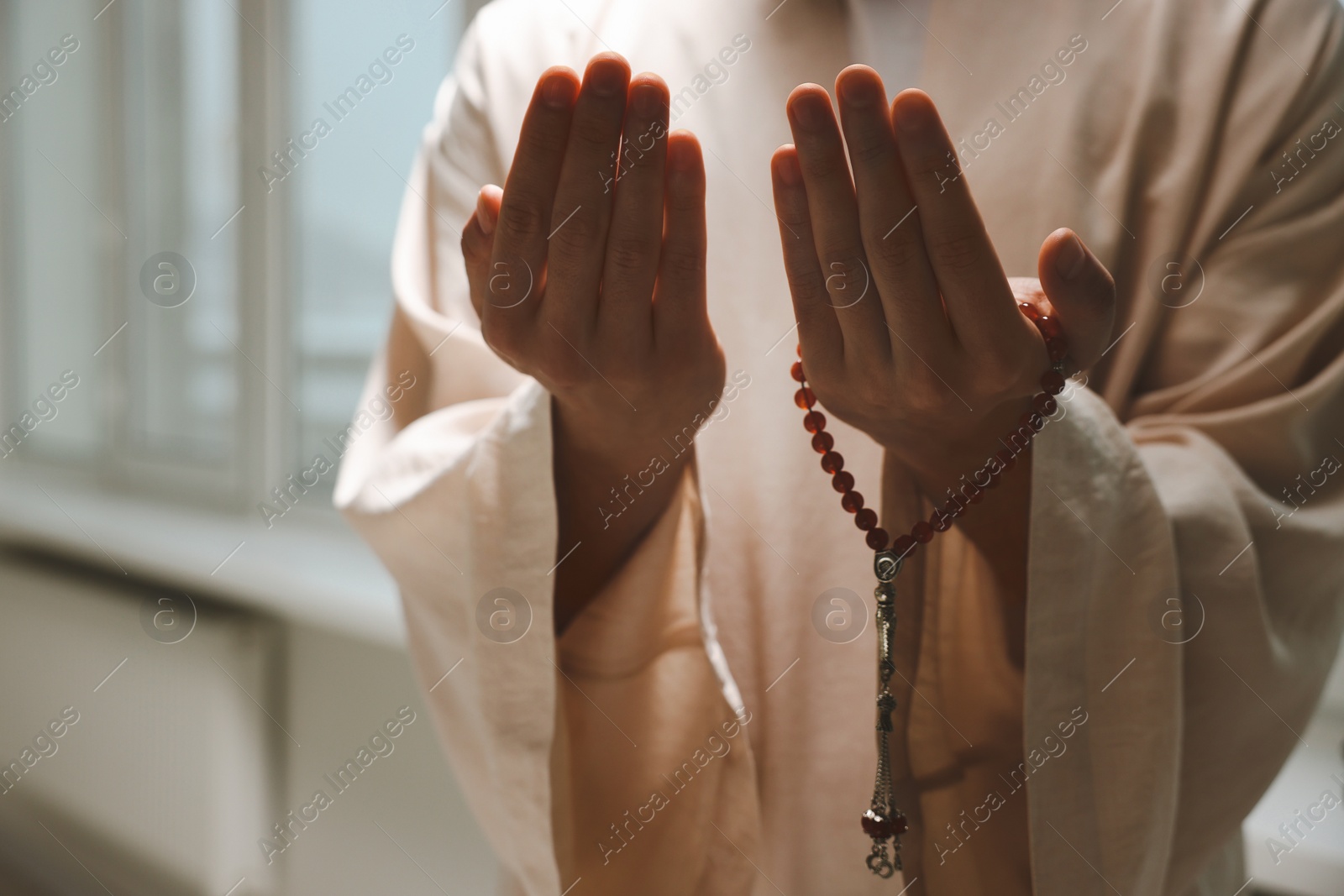 Photo of Muslim man with misbaha praying near window indoors, closeup. Space for text