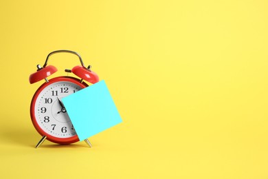 Photo of Alarm clock and blank reminder note on yellow background, space for text