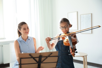 Young woman teaching little girl to play violin indoors