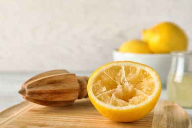 Wooden board with lemon reamer and squeezed fruit on table