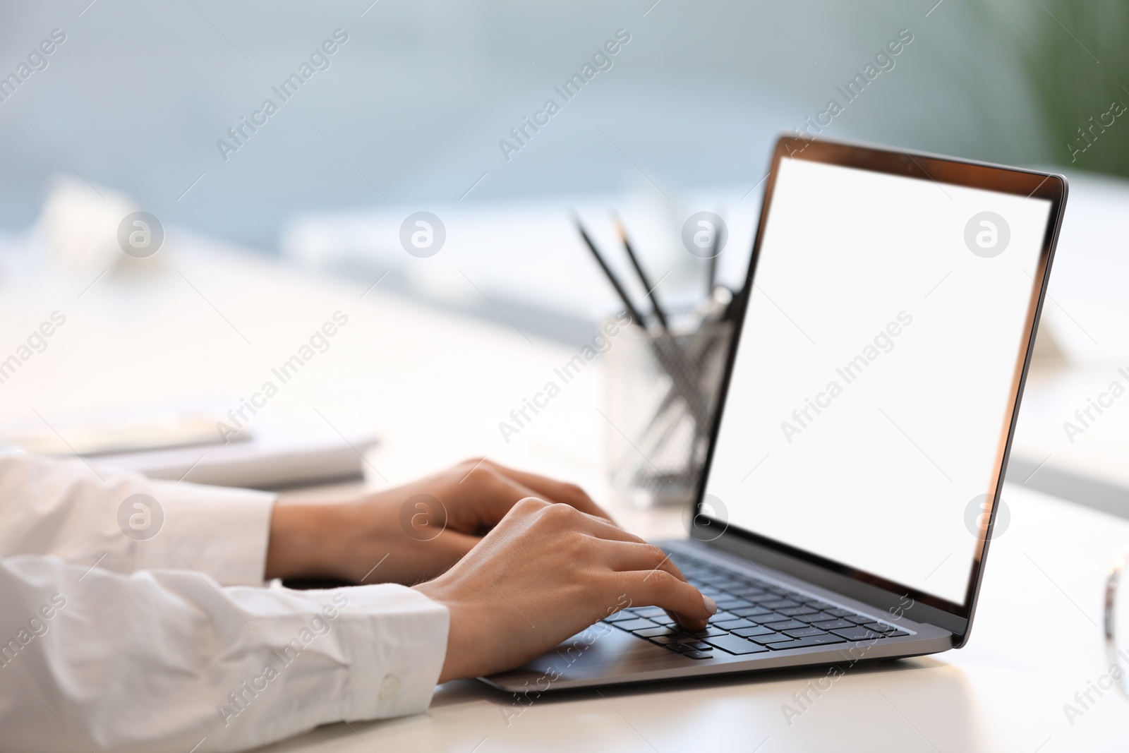 Photo of Woman using modern laptop at white desk in office, closeup