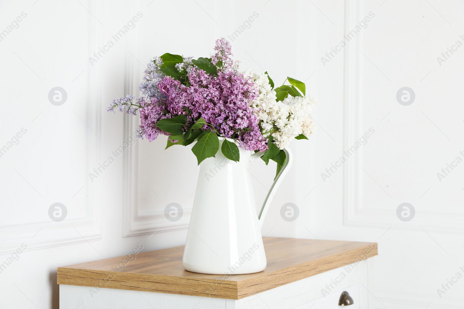 Photo of Beautiful lilac flowers in vase on wooden table near white wall