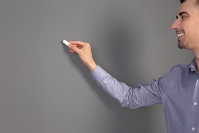 Young male teacher with chalk on grey background