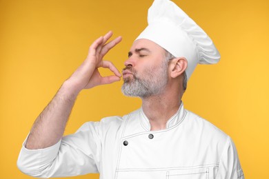 Photo of Chef in uniform showing perfect sign on orange background