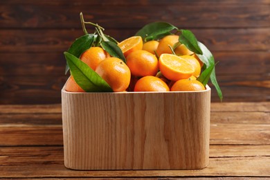 Fresh tangerines with green leaves in crate on wooden table