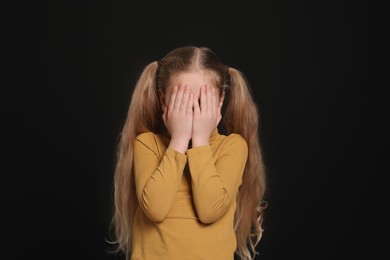 Girl covering face with hands on black background. Children's bullying
