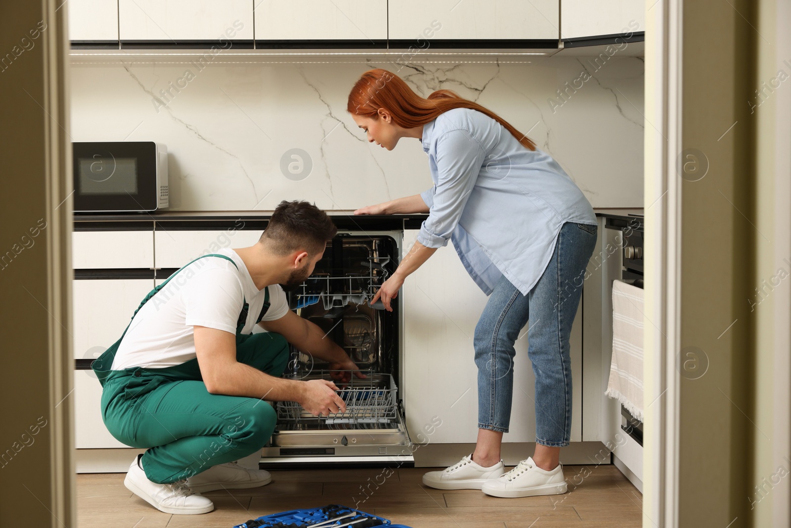 Photo of Woman looking how serviceman repairing her dishwasher in kitchen