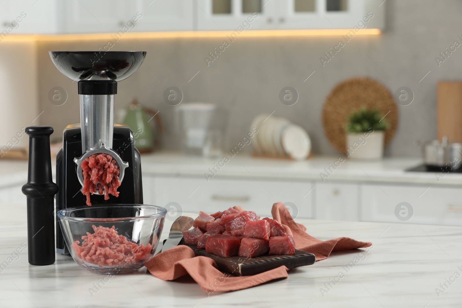 Photo of Electric meat grinder with beef mince on white table in kitchen, space for text