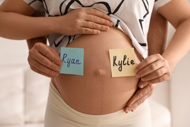Photo of Man and pregnant woman with different baby names on belly indoors, closeup