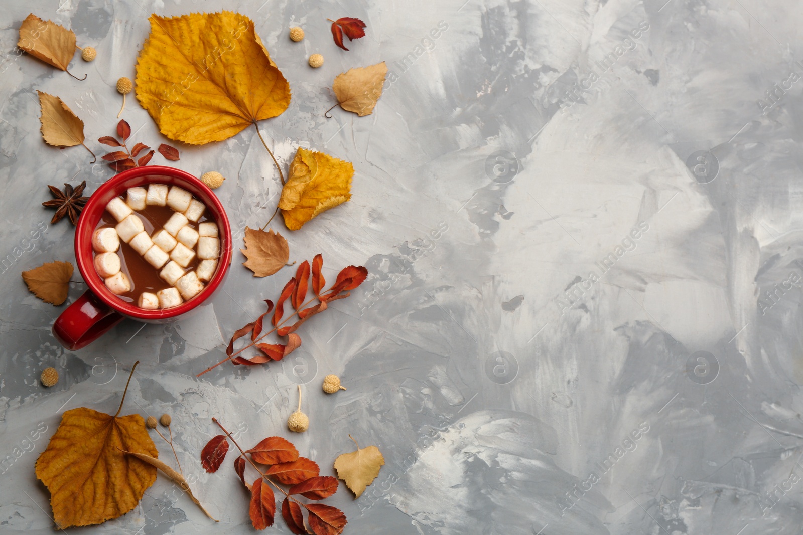 Photo of Flat lay composition with cup of hot drink and autumn leaves on grey table, space for text. Cozy atmosphere