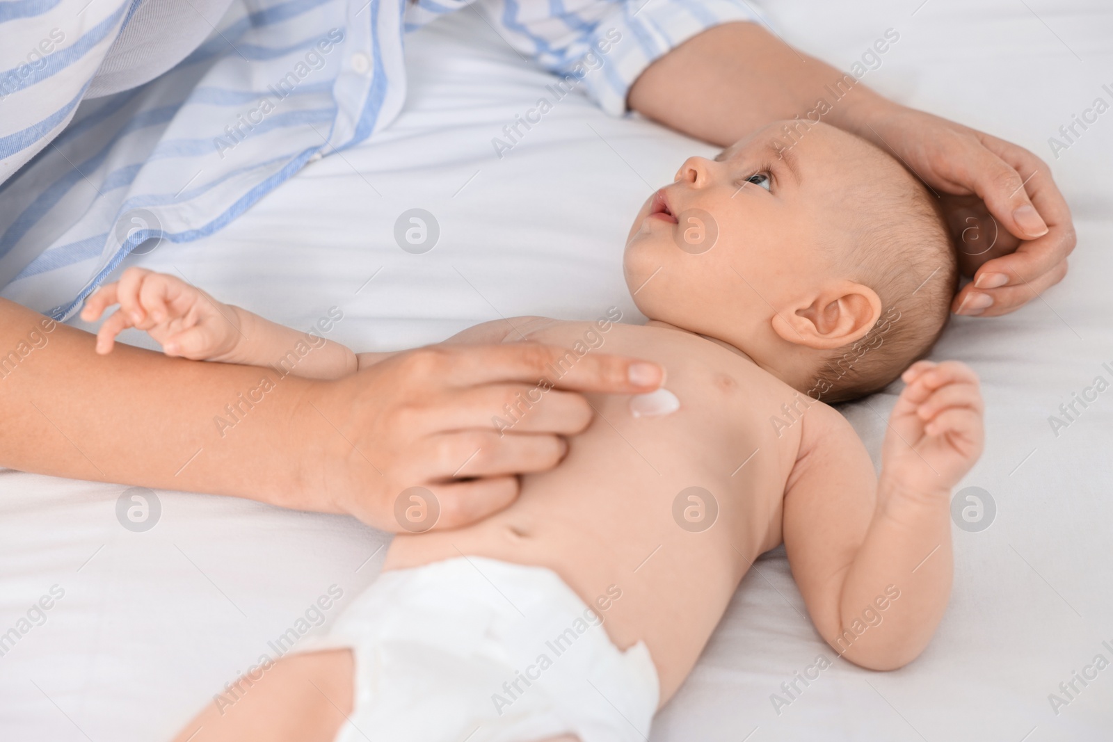 Photo of Woman applying body cream onto baby`s skin on bed, closeup