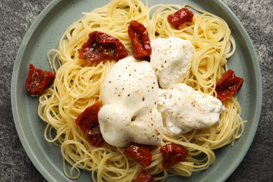 Photo of Delicious spaghetti with burrata cheese and sun dried tomatoes on grey table, top view