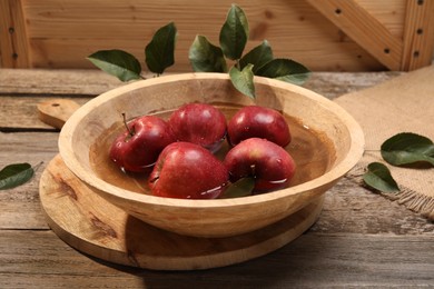 Fresh red apples in bowl with water and leaves on wooden table