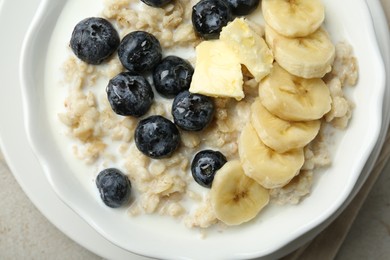 Photo of Tasty oatmeal with banana, blueberries, butter and milk served in bowl on light grey table, top view