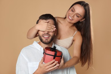 Photo of Woman presenting gift to her boyfriend on beige background