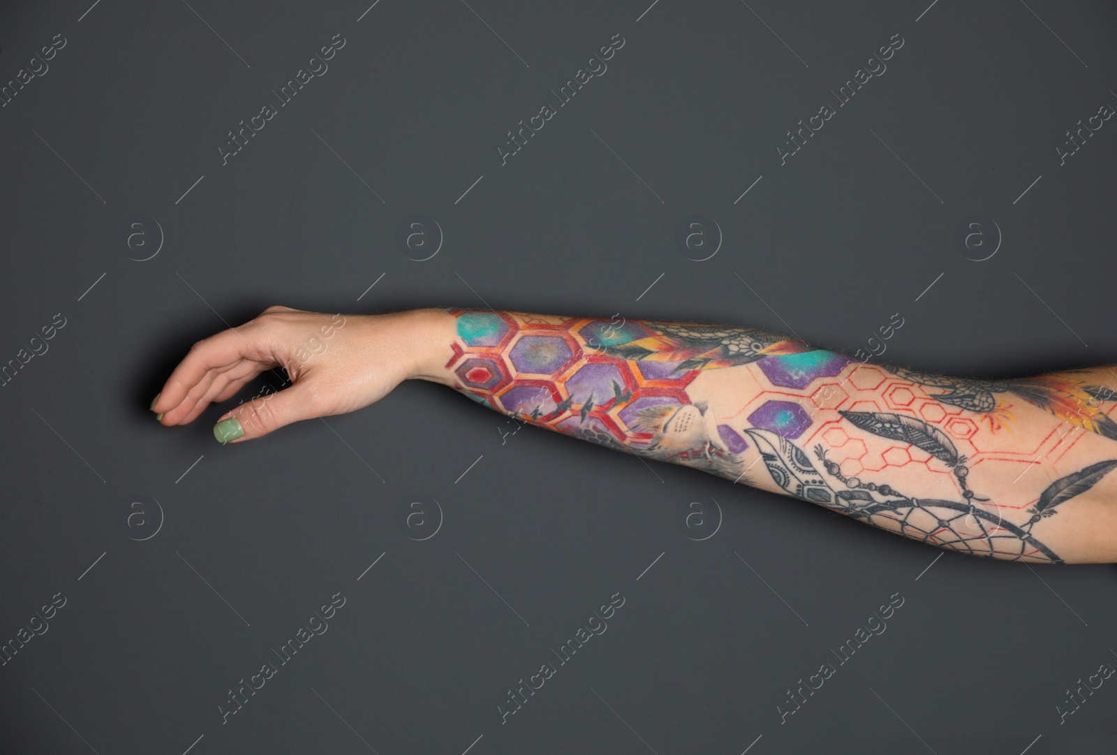 Photo of Woman with colorful tattoos on arm against dark grey background, closeup