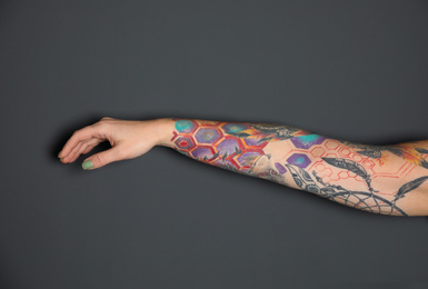 Woman with colorful tattoos on arm against dark grey background, closeup