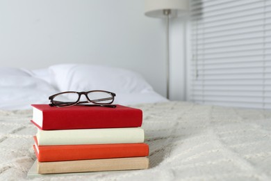 Photo of Books and glasses on white soft blanket in bedroom, space for text