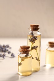 Photo of Essential oil and lavender flowers on white wooden table, closeup