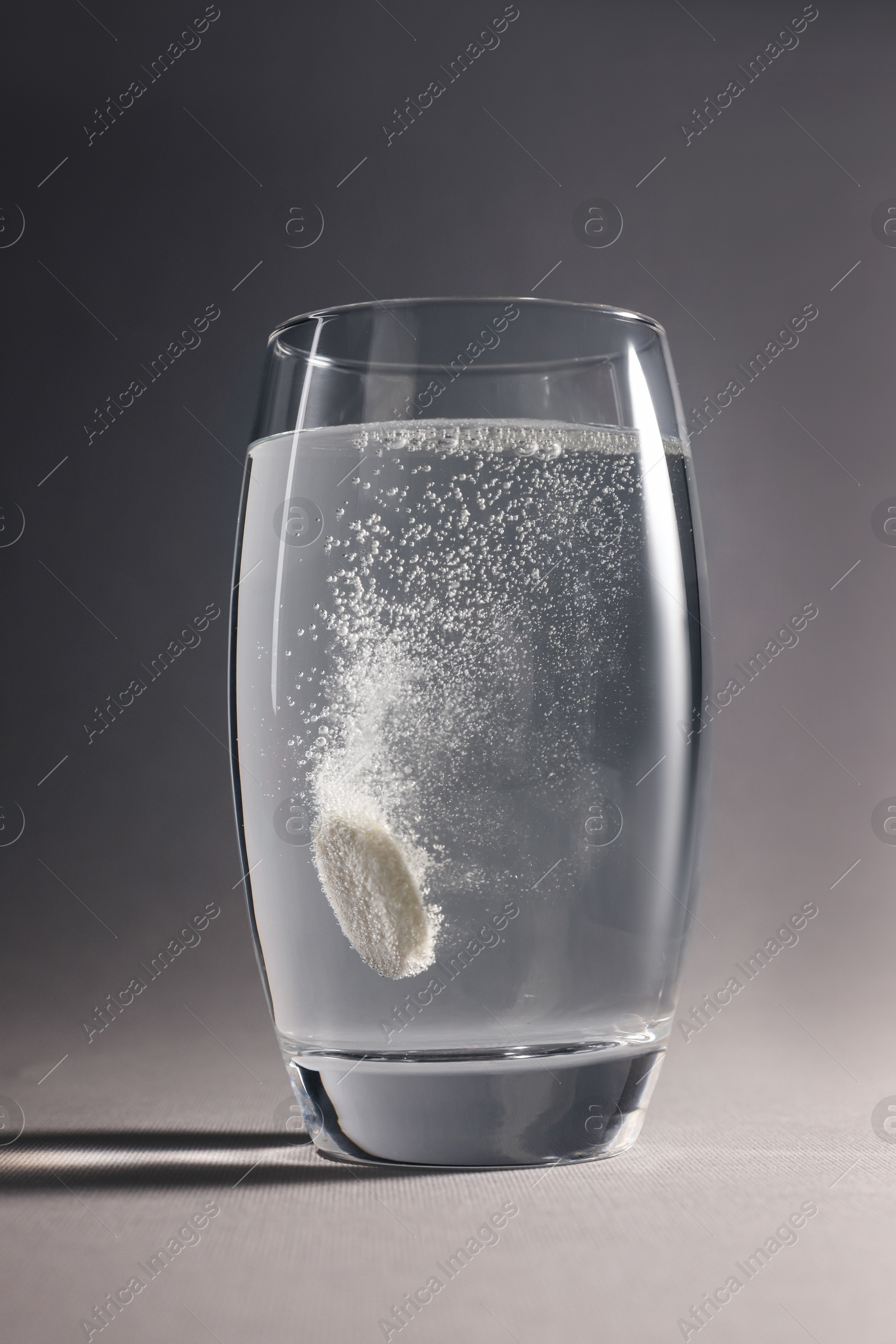 Photo of Effervescent pill dissolving in glass of water on grey background