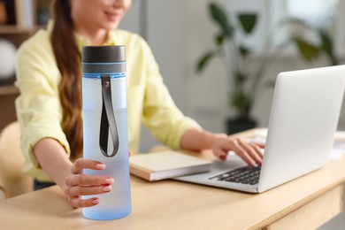 Woman holding transparent bottle at workplace indoors, closeup. Space for text