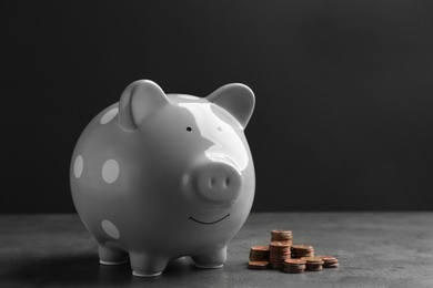 Photo of Piggy bank and coins on table against dark background. Space for text