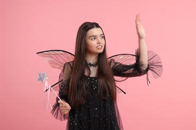 Photo of Beautiful girl in fairy costume with wings and magic wand on pink background