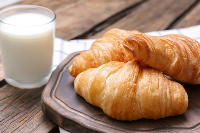 Photo of Wooden board with tasty croissants and glass of milk on table