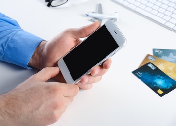 Photo of Man using mobile phone at table in travel agency, closeup. Space for design
