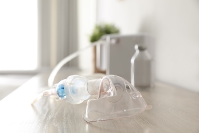 Face mask near modern nebulizer on wooden table indoors. Inhalation equipment
