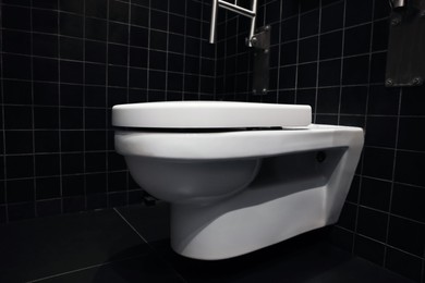 Photo of Clean ceramic toilet bowl near tiled wall indoors