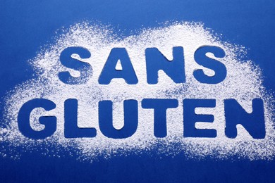 Photo of Phrase Gluten free written in French with flour on blue background, top view