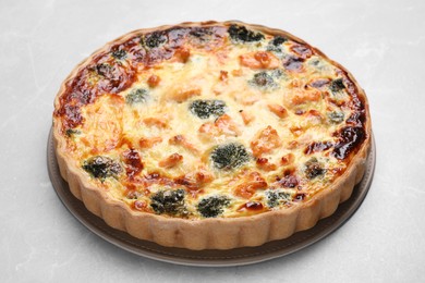 Delicious homemade quiche with salmon and broccoli on light gray table