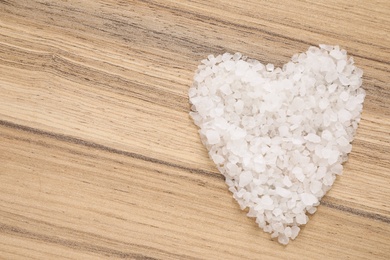 Photo of Heart shaped pile of sea salt for spa scrubbing procedure on wooden background, top view