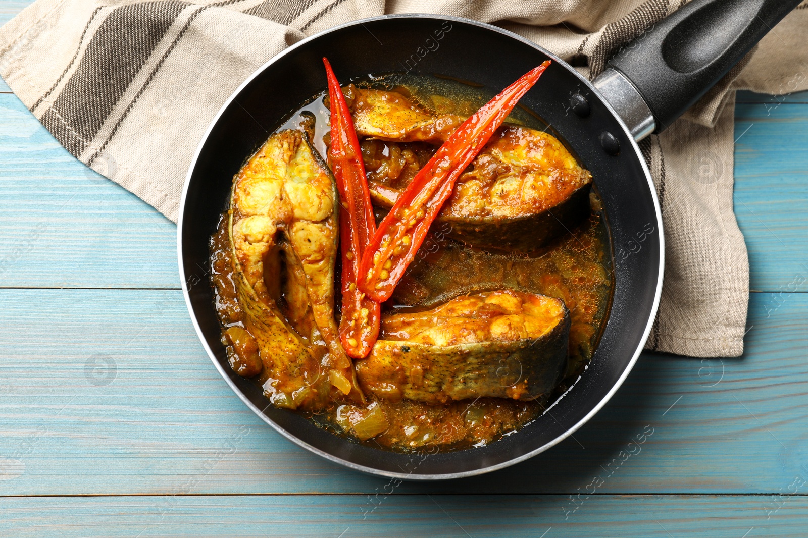 Photo of Tasty fish curry in frying pan on light blue wooden table, top view. Indian cuisine