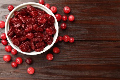 Tasty dried cranberries in bowl and fresh ones on wooden table, top view. Space for text