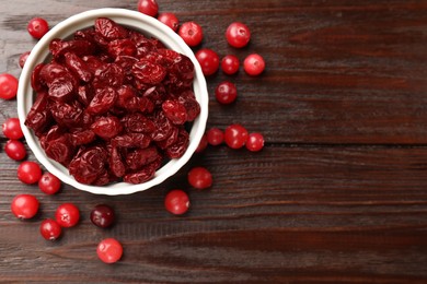 Photo of Tasty dried cranberries in bowl and fresh ones on wooden table, top view. Space for text